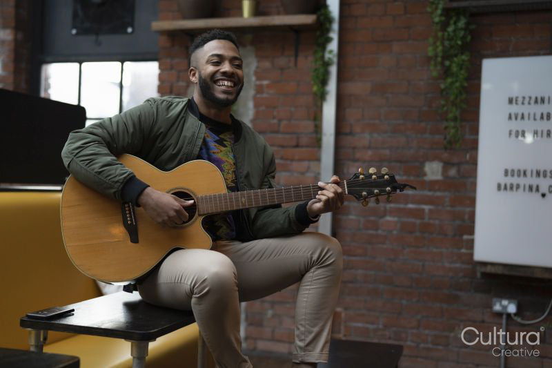 Young man playing acoustic guitar in office lounge