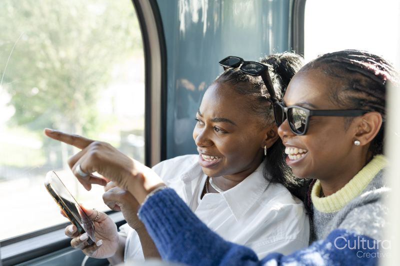 Young female friends riding city bus and using phone