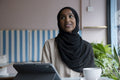 Smiling young woman in hijab working on tablet in cafe