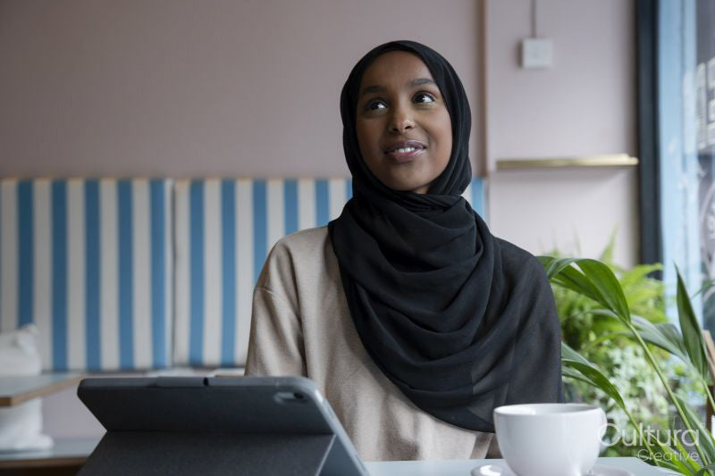 Smiling young woman in hijab working on tablet in cafe