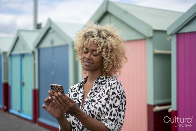 Smiling woman using smart phone near beach huts
