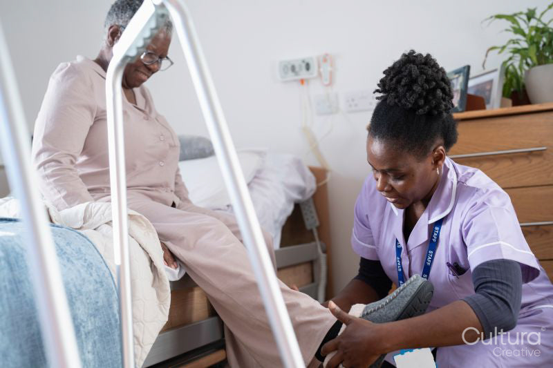 Caregiver helping senior woman sitting on bed to put on slippers