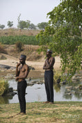 Two young shirtless men standing on riverbank