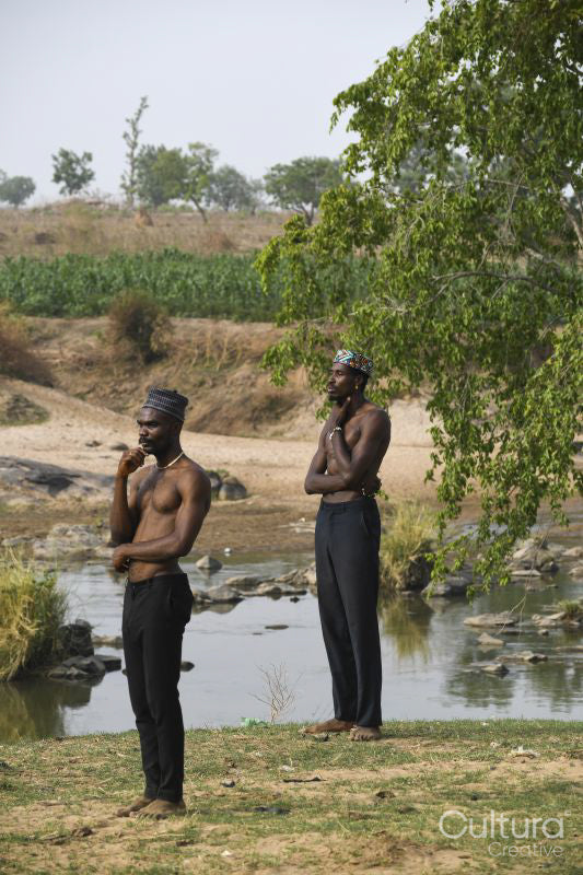 Two young shirtless men standing on riverbank