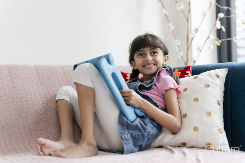 Little girl using tablet while sitting on sofa