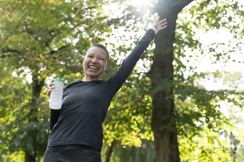 Portrait of smiling athletic woman with arm raised in park