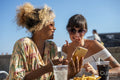 Female couple eating french fries and using phone
