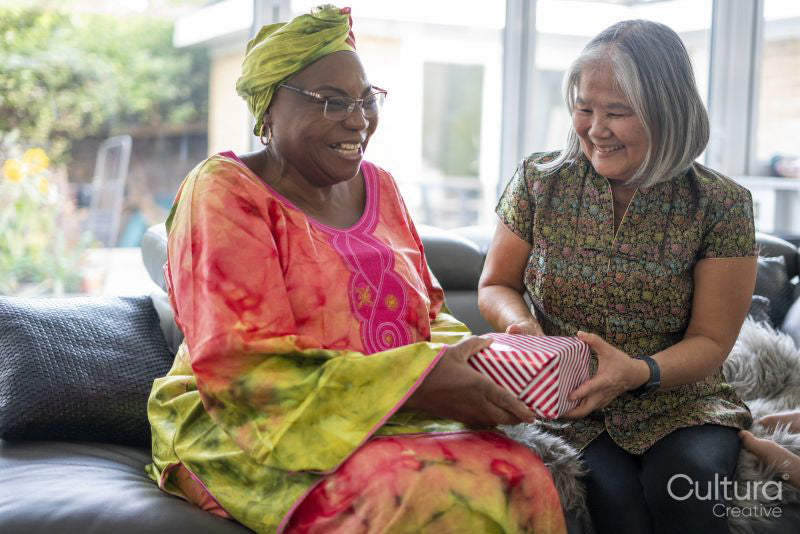 Woman giving boxed gift to another woman in living room