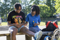 Teenage girl in wheelchair with friend applying sunscreen in park
