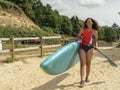 Smiling woman carrying paddleboard and oar on beach