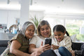 Two women and girl sitting on sofa looking at smartphone