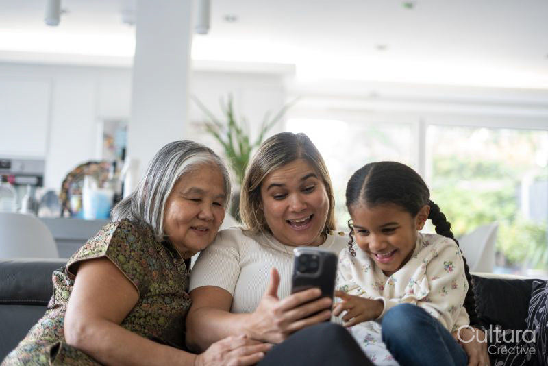 Two women and girl sitting on sofa looking at smartphone