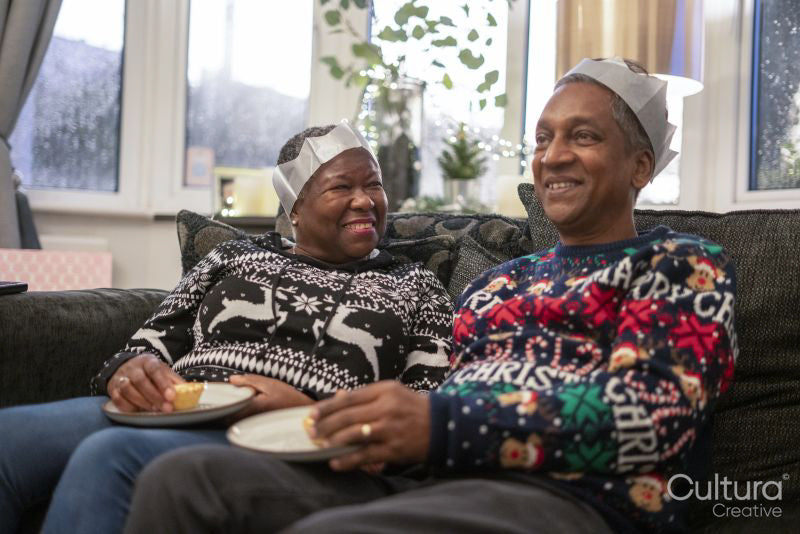 Senior couple sitting on sofa wearing Christmas decorations