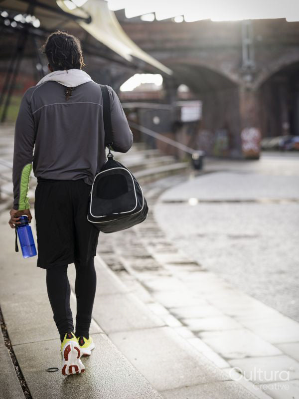 Rear view of athletic man with gym bag walking outdoors
