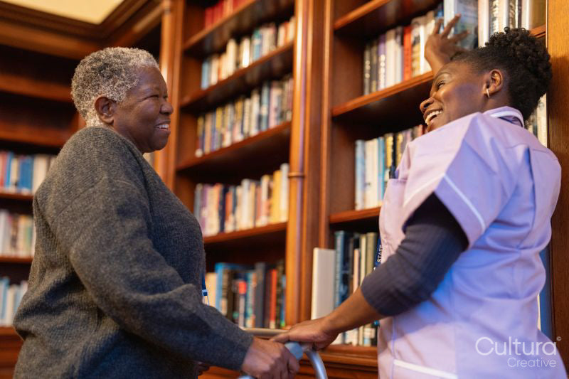 Senior woman and nurse picking books from library in nursing home