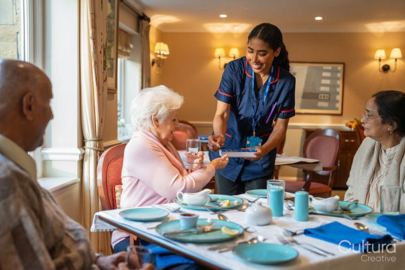Nurse visiting group of seniors dining at cafeteria in nursing home