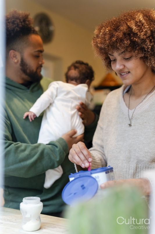 Father holding baby daughter and mother preparing baby food at home