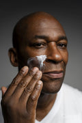 Portrait of man applying face cream against gray background