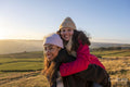 Young woman giving friend piggyback ride in rural landscape