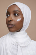 Studio shot of young woman in white hijab applying face cream