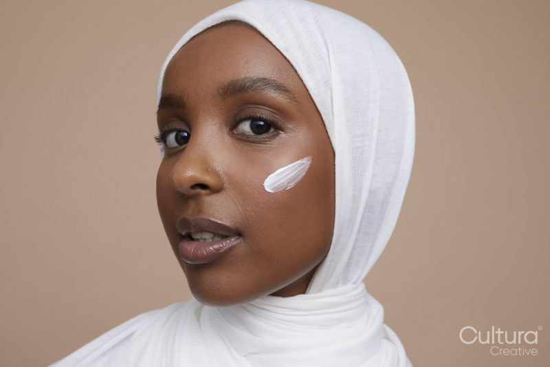 Studio portrait of young woman in white hijab applying face cream