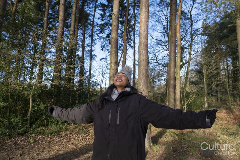 Smiling young woman with outstretched arms in forest