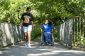 Teenage girl in wheelchair with friend walking in park