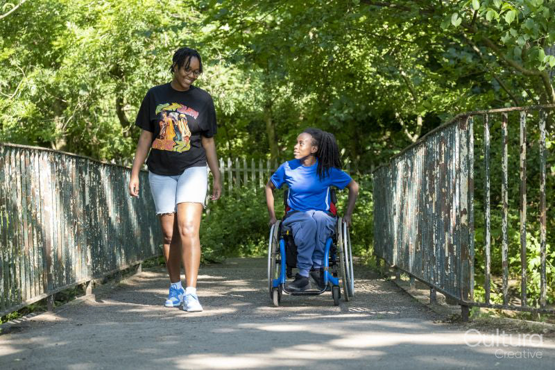 Teenage girl in wheelchair with friend walking in park