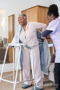 Caregiver helping smiling senior woman putting on bathrobe in bedroom