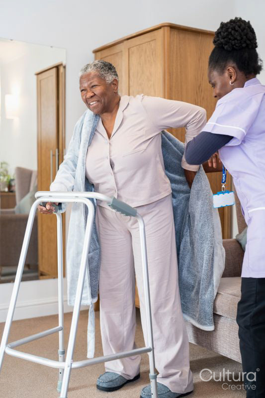 Caregiver helping smiling senior woman putting on bathrobe in bedroom