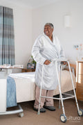 Smiling senior woman in bathrobe standing with mobility walker in bedroom