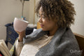 Woman wrapped in shawl reading book and holding cup