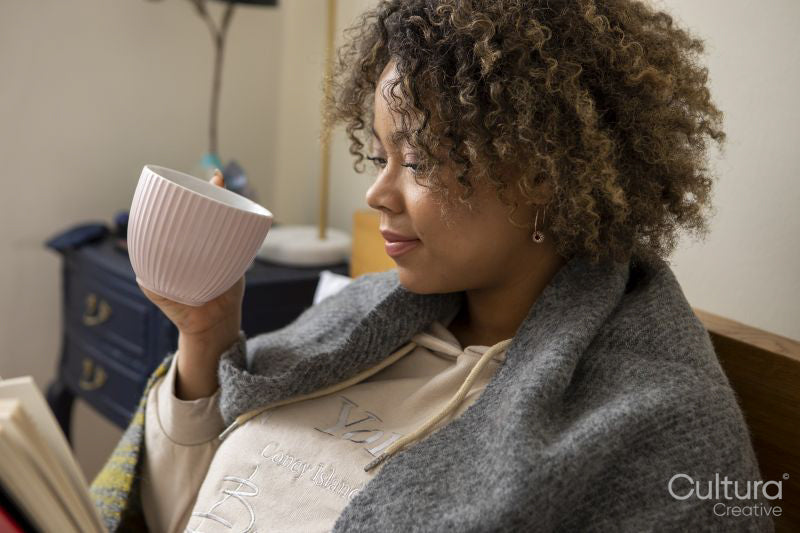 Woman wrapped in shawl reading book and holding cup