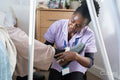 Caregiver helping senior woman sitting on bed to put on slippers