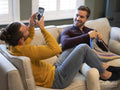 Man photographing boyfriend while knitting at home