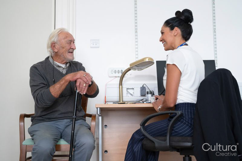 Smiling senior patient talking to female doctor at desk in office