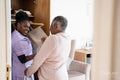 Smiling caregiver assisting senior woman choosing pants at closet