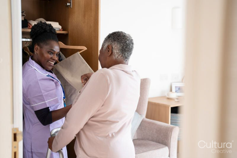 Smiling caregiver assisting senior woman choosing pants at closet