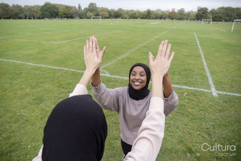 Two smiling women in hijabs giving high five in soccer field