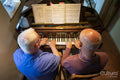 Senior male couple playing piano at home