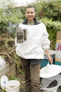 Portrait of smiling female beekeeper holding smoker in urban garden