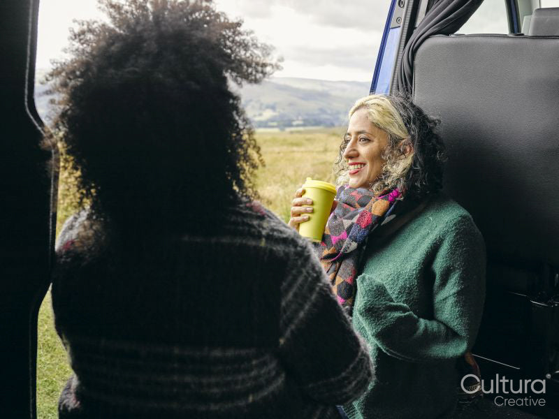Smiling women sitting in van and drinking from cup