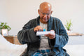 Senior man taking pills while sitting on bed in room at nursing home