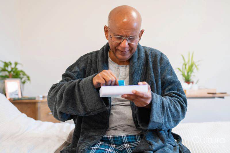 Senior man taking pills while sitting on bed in room at nursing home