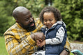 Smiling man with daughter on laps sitting on bench in park