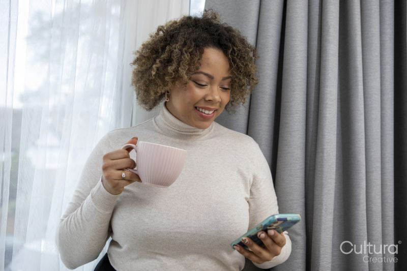 Smiling woman holding coffee cup and looking at smart phone