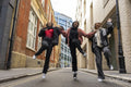 Three young women wearing hijabs holding hands and jumping in city