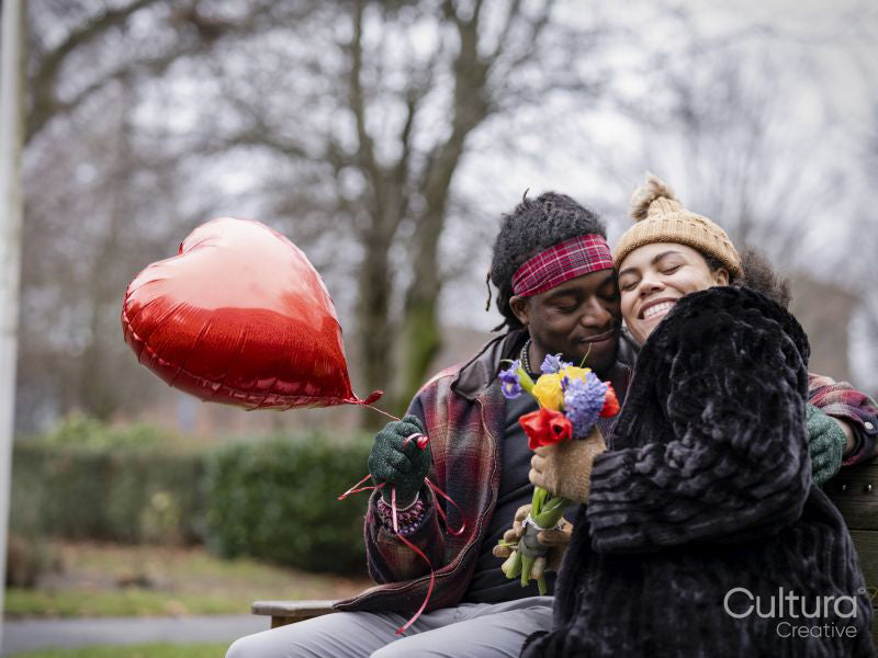 Smiling couple with heart shaped balloon and flowers in park