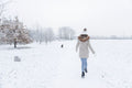 Rear view of woman walking in snowy field with dog