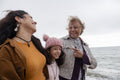 Grandmother, mother and daughter laughing while walking on beach on cloudy day
